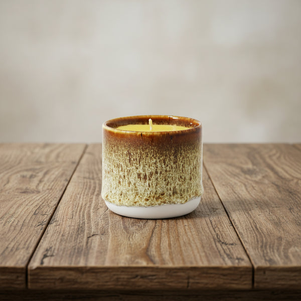 Bienenwachskerze im braunen Keramikbecher auf dem Tisch